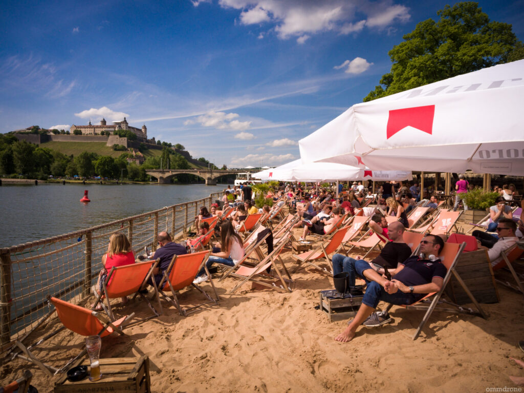 Der große Sandbereich des Stadtstrand Würzburgs mit vielen Sonnenliegen im Strand.