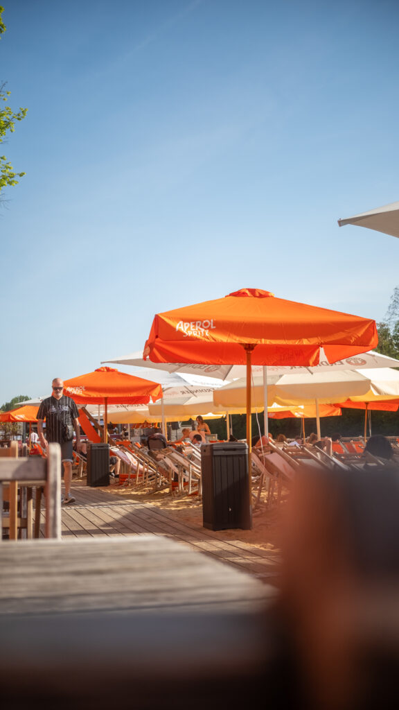 Sonnige Strandatmosphäre mit Liegestühlen und Aperol-Sonnenschirmen auf dem Stadtstrand Würzburg am Tag