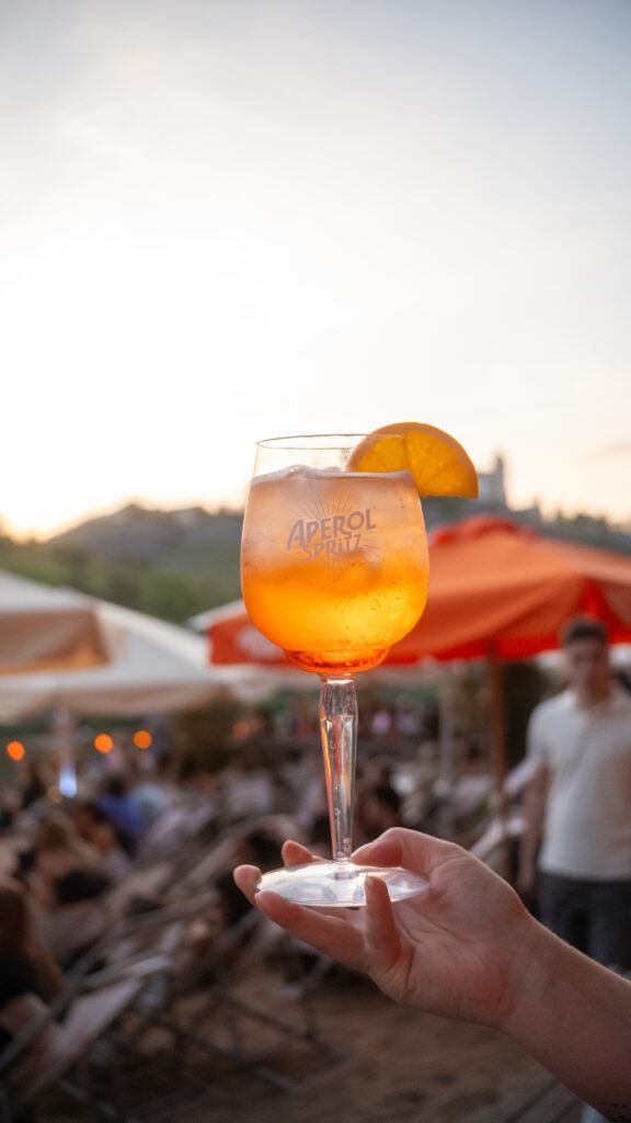 Ein Glas Aperol Spritz vor Sonnenuntergang am Stadtstrand Würzburg mit Blick auf die Festung Marienberg